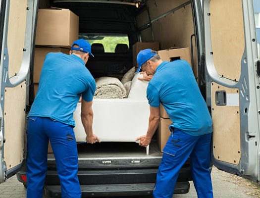 Two Male Workers In Blue Uniform Adjusting Sofa In Truck